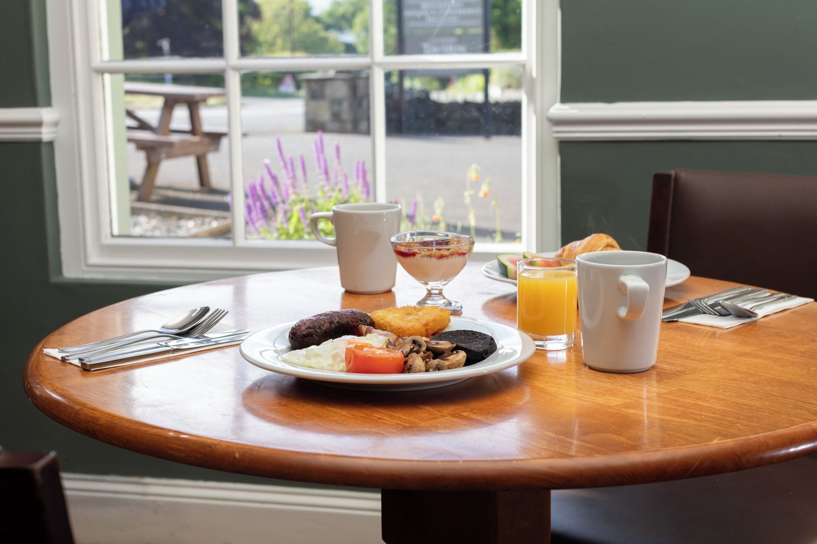 A breakfast table with a plate of food, a glass of orange juice, and a mug.