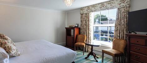 Een hotelkamer met een groot bed, twee fauteuils, een tafeltje, een dressoir en een televisie.