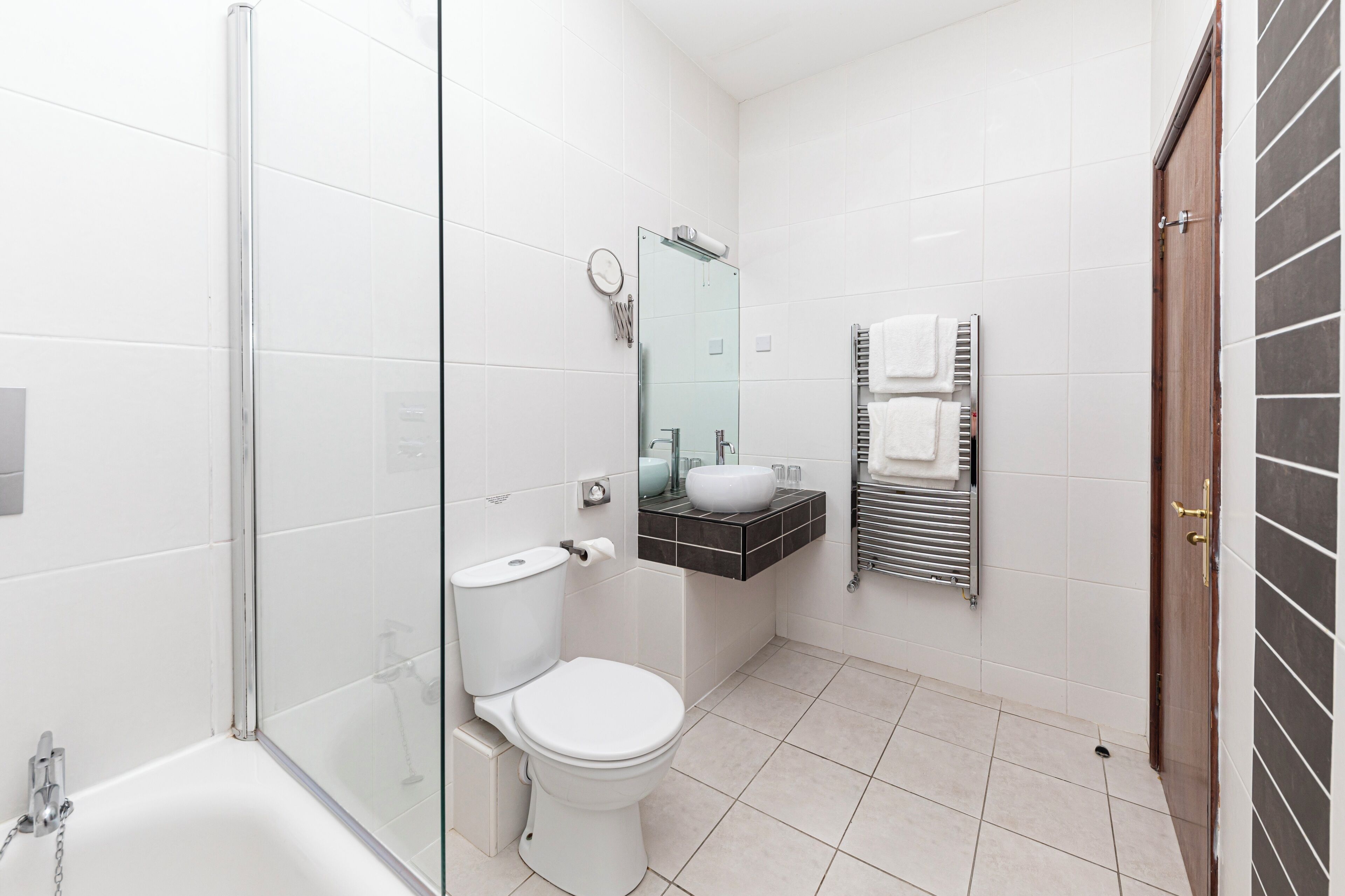 Ein modernes Badezimmer mit Glasdusche, weißer Toilette, Waschbecken mit Spiegel und Handtuchhalter.