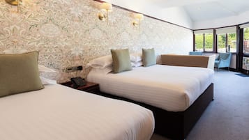 A hotel room with two beds, a large window, and a patterned wallpaper.