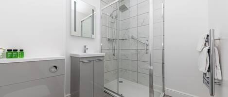A modern bathroom with a glass-enclosed shower, a white sink, and a mirror above it.