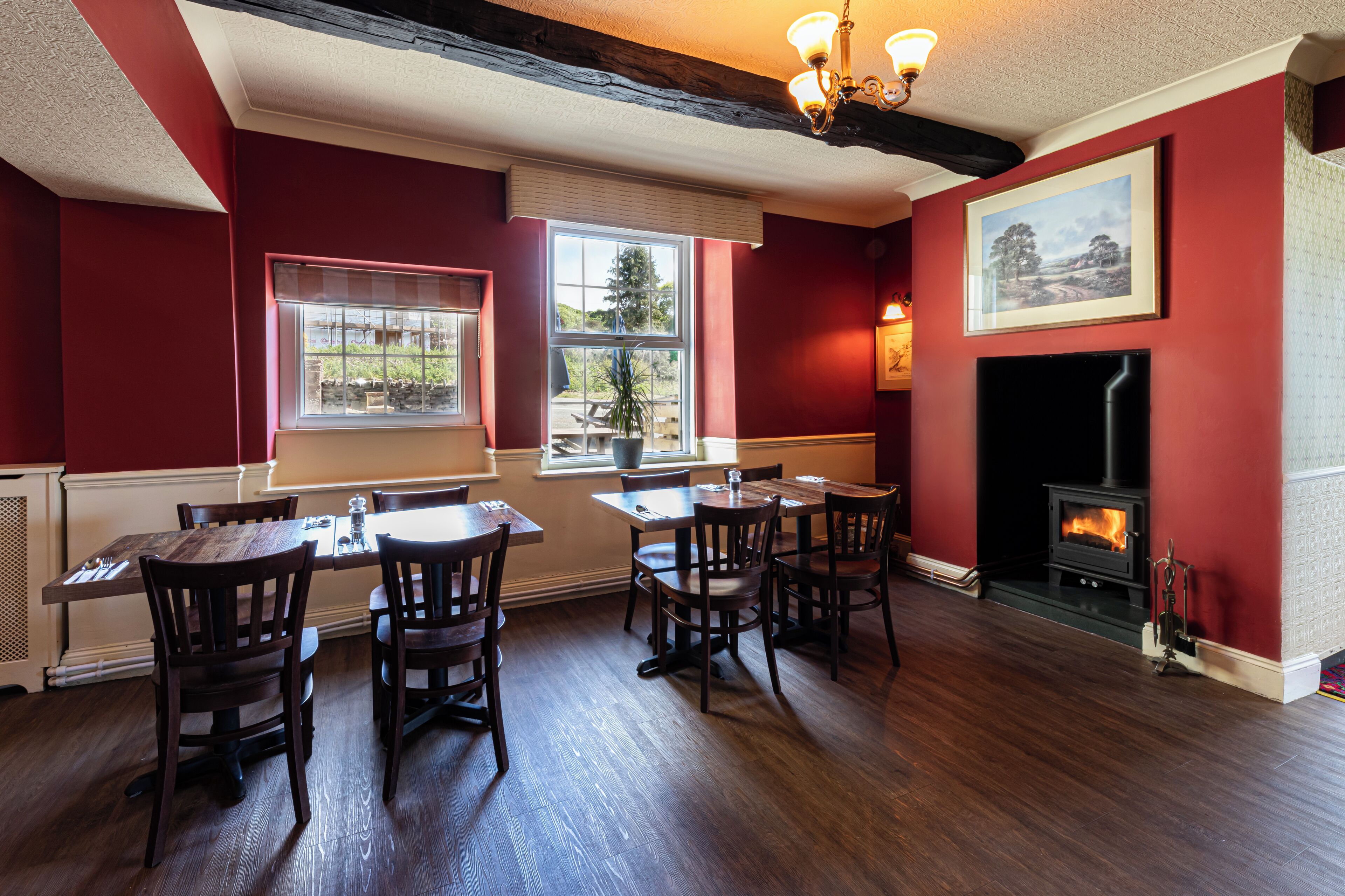 A dining area with wooden tables and chairs, a fireplace, and a large window with a view of greenery.