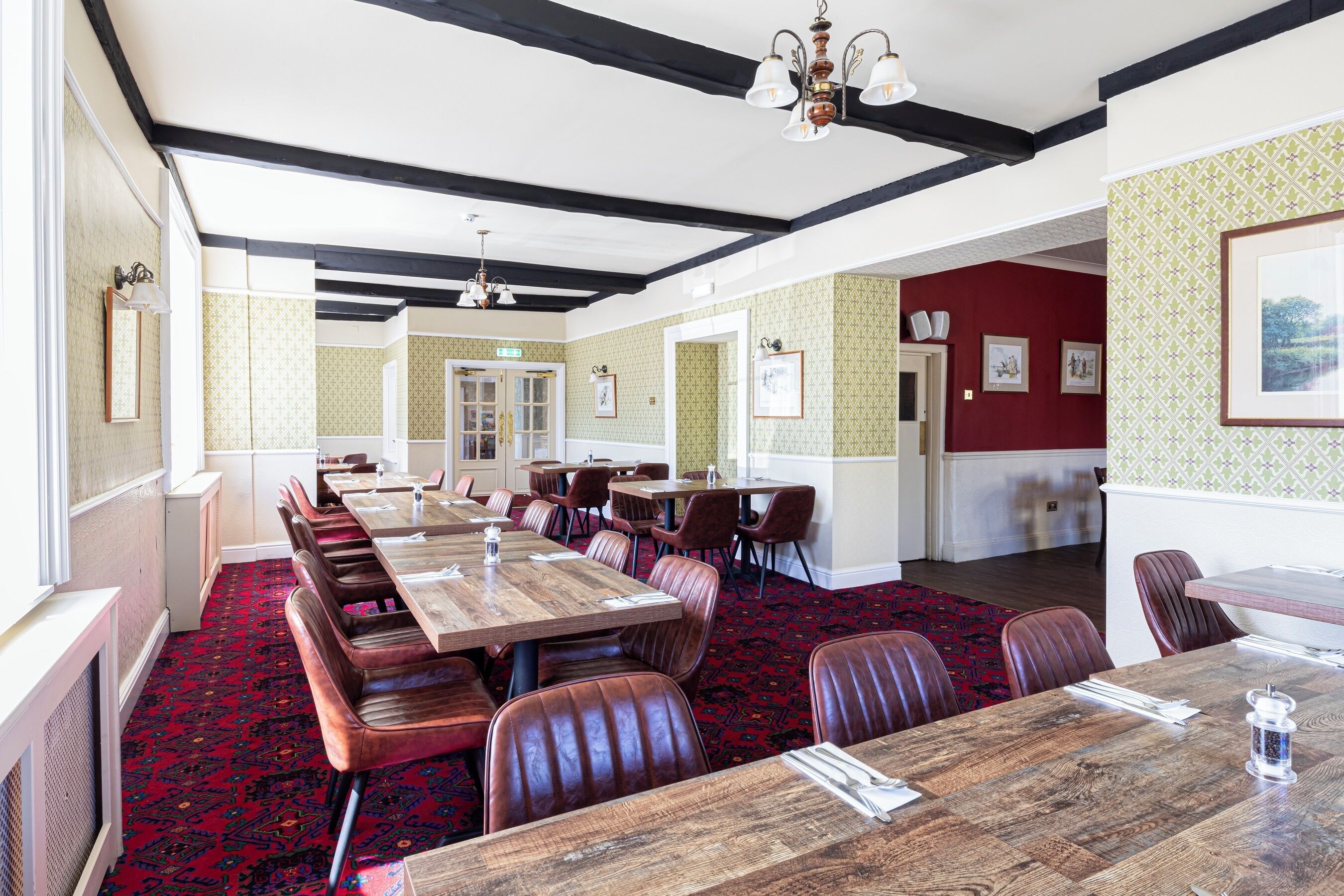 A dining area with long wooden tables and leather booths, a patterned carpet, and a red accent wall.