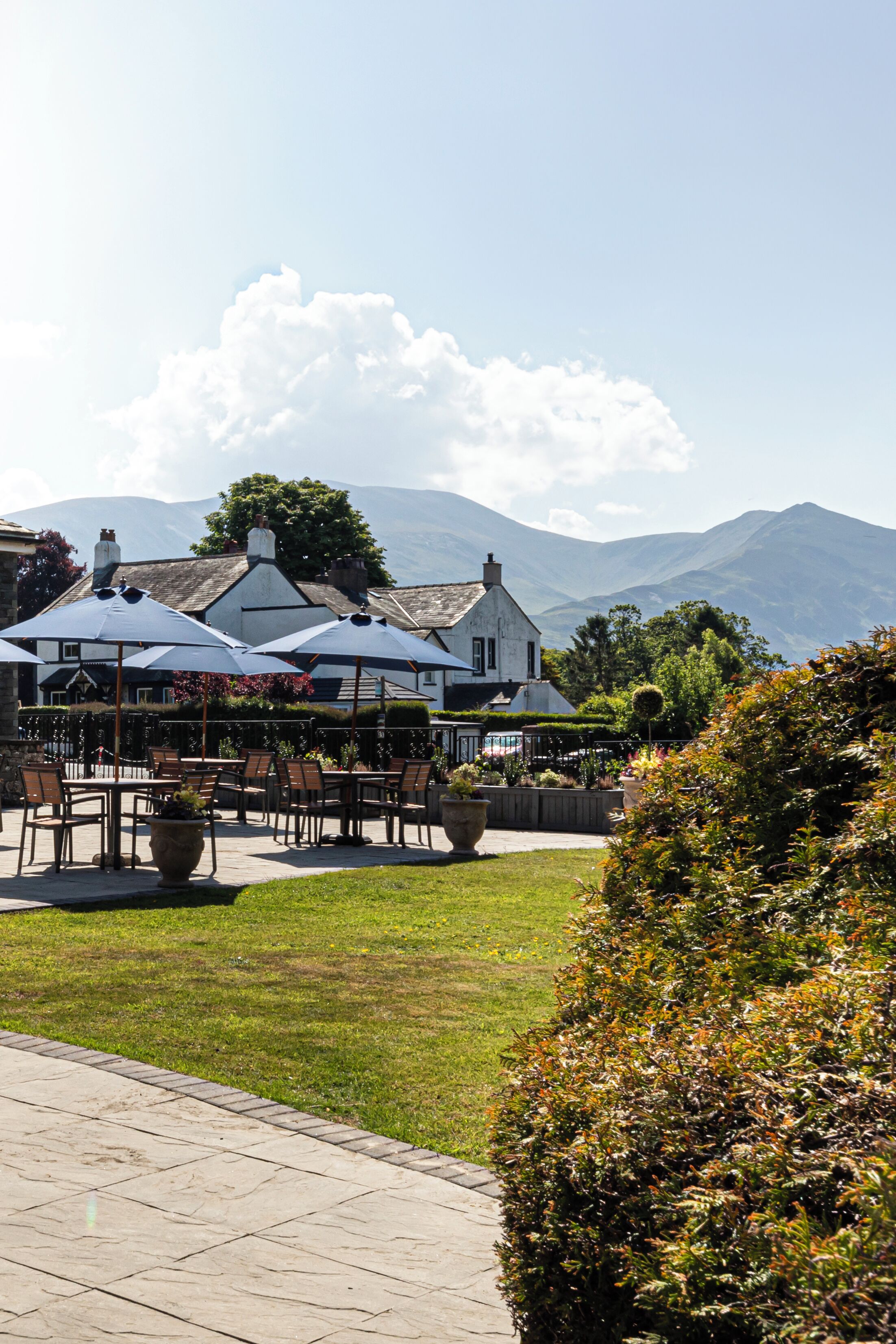 An outdoor seating area with umbrellas, tables, and chairs, overlooking a mountainous landscape.