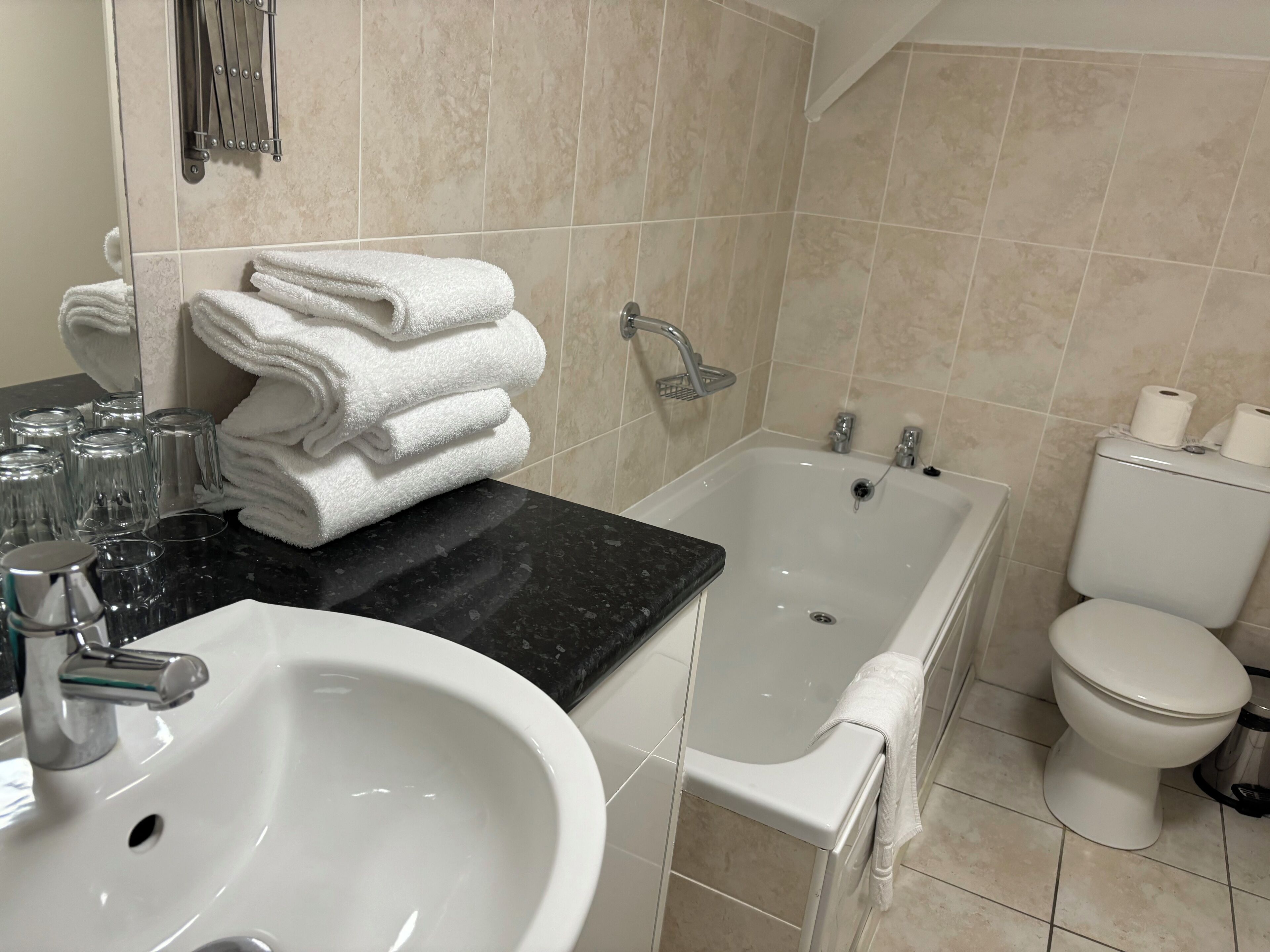 A bathroom with a sink, a bathtub, and a toilet. There are towels stacked on the counter, and a showerhead is visible.