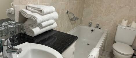 A bathroom with a sink, a bathtub, and a toilet. There are towels stacked on the counter, and a showerhead is visible.