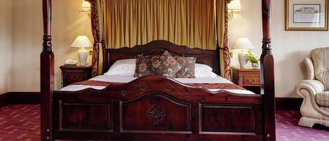 Un lit à baldaquin à quatre poteaux avec une tête de lit en bois, deux tables de chevet avec des lampes, une chaise et un tableau encadré au mur.