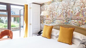A hotel room with a large bed, two mustard-colored pillows, a nightstand with a telephone, and a window with a yellow curtain.