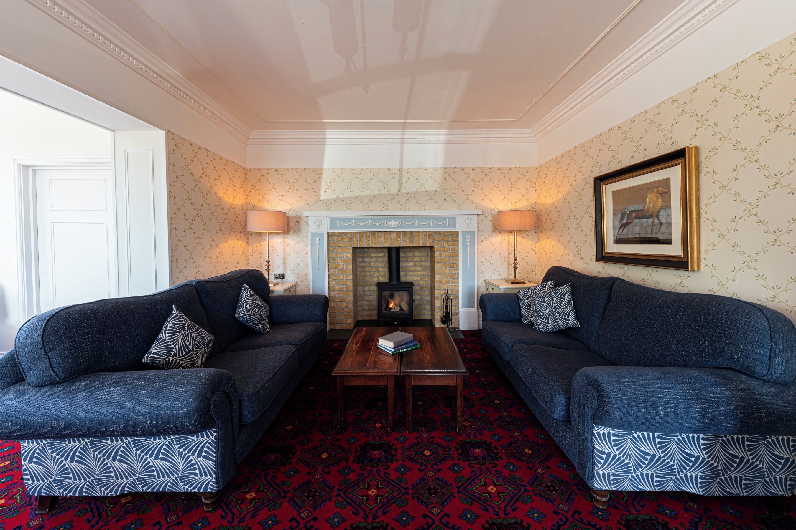 A room with two sofas, a fireplace, and patterned wallpaper.