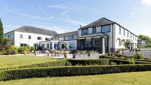 A hotel with a patio area featuring outdoor seating and umbrellas, surrounded by well-maintained gardens and hedges.