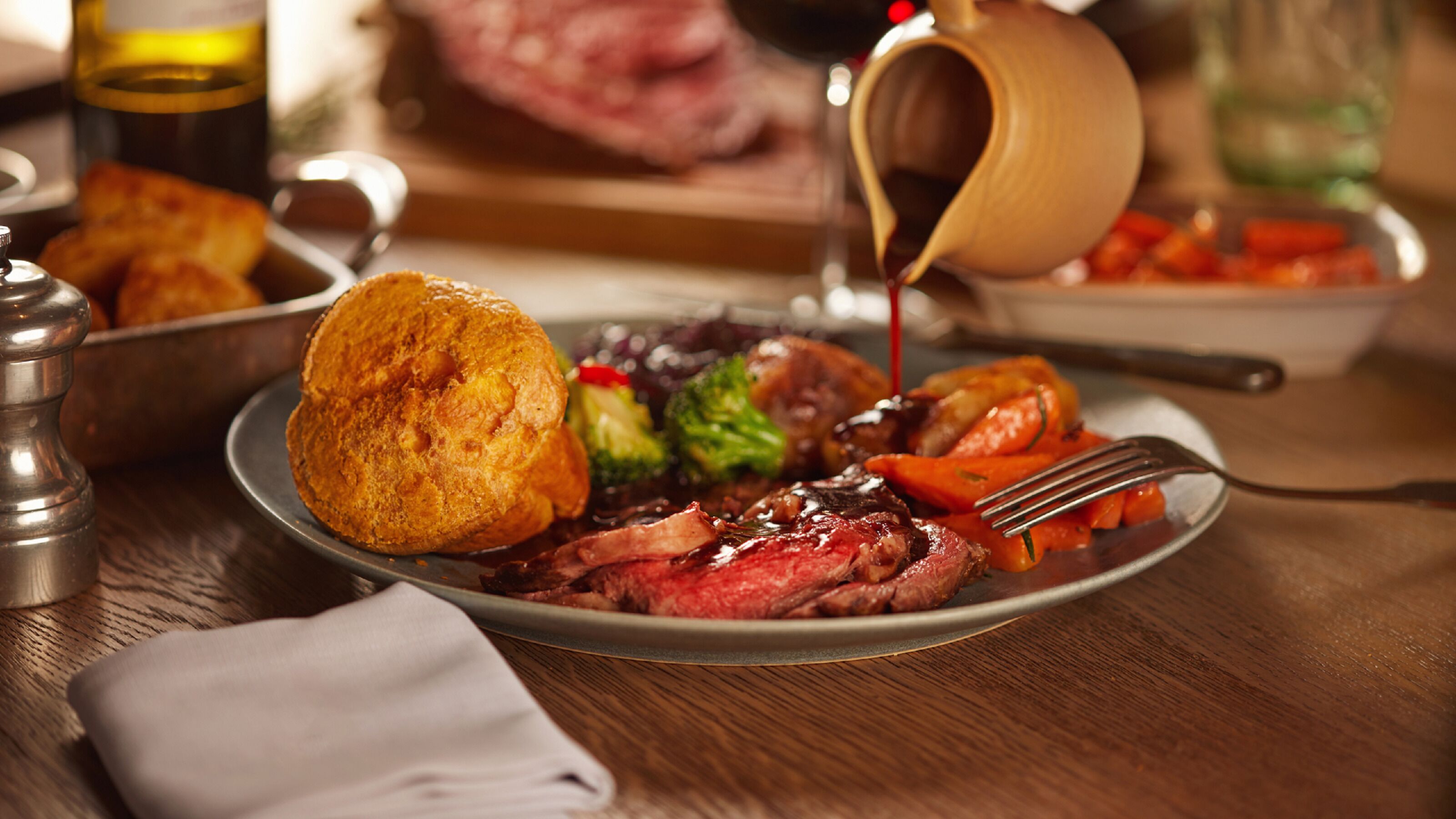 A plate of food with a roasted meat, vegetables, and a biscuit.