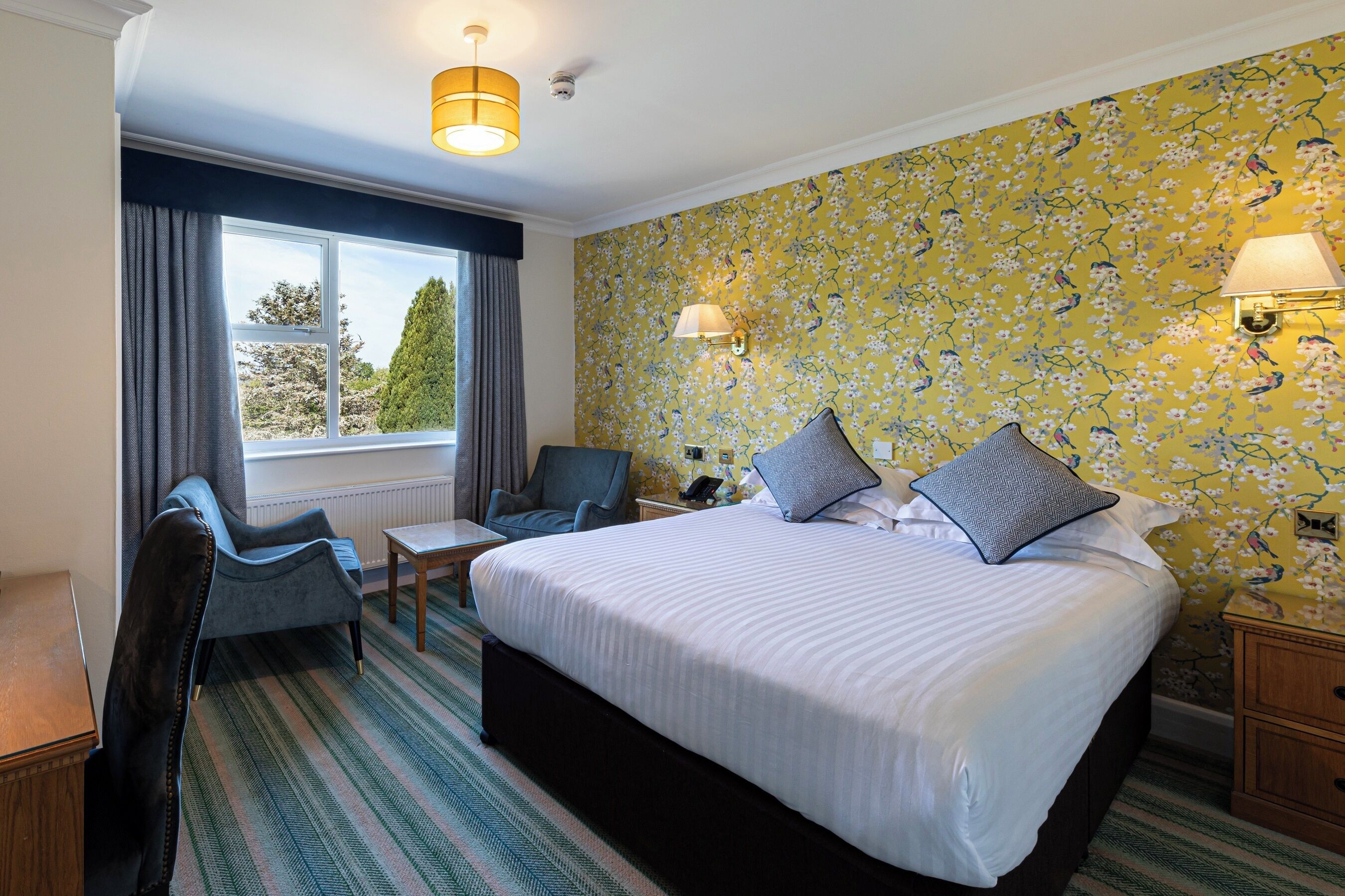 A hotel room with a large bed, two armchairs, a small table, and a window with curtains.