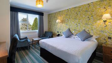 A hotel room with a large bed, two armchairs, a small table, and a window with curtains.