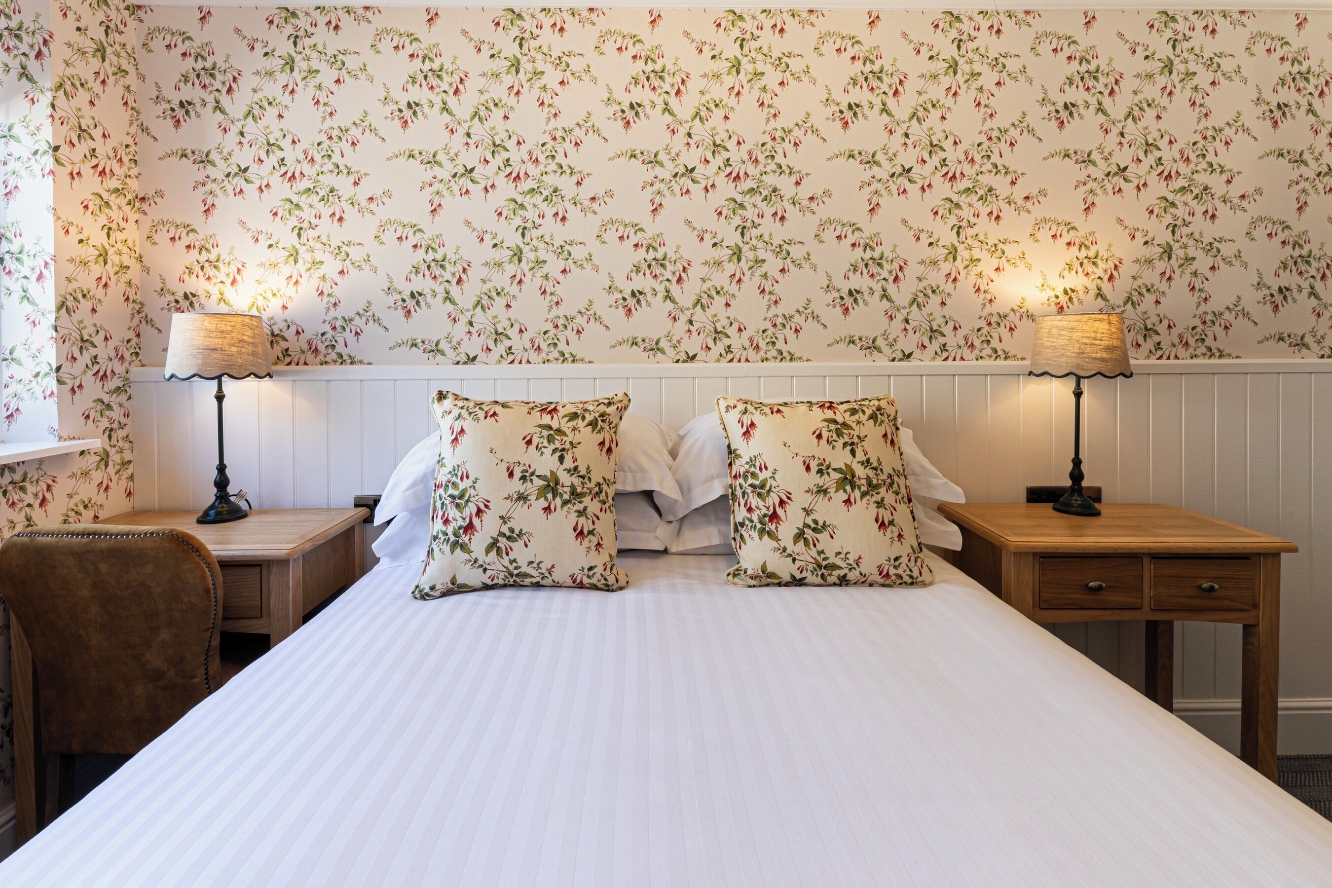A neatly made bed with floral-patterned pillows, two bedside tables with lamps, and a chair.