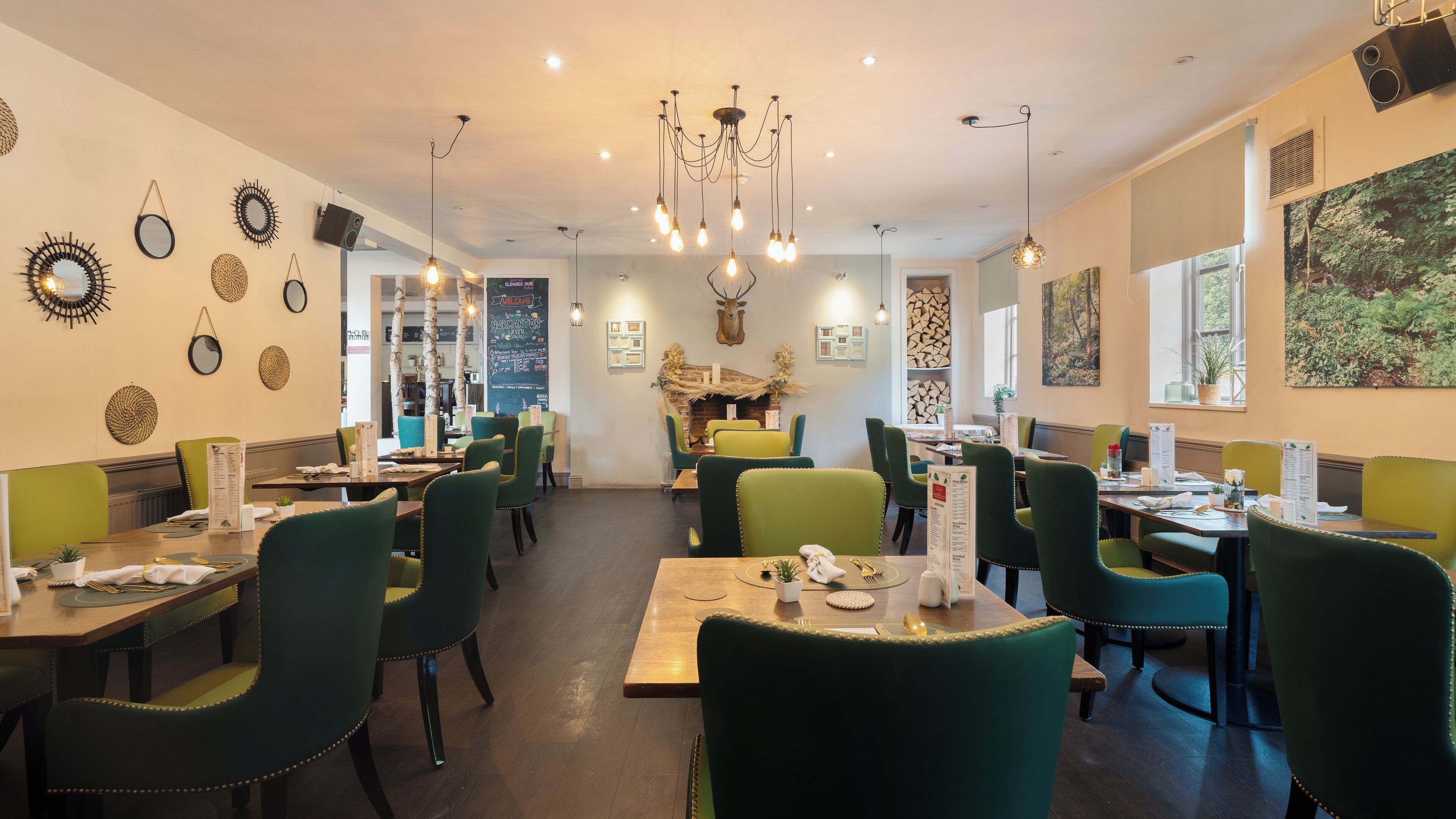 A restaurant with green upholstered chairs, wooden tables, a fireplace, and a variety of wall decorations.