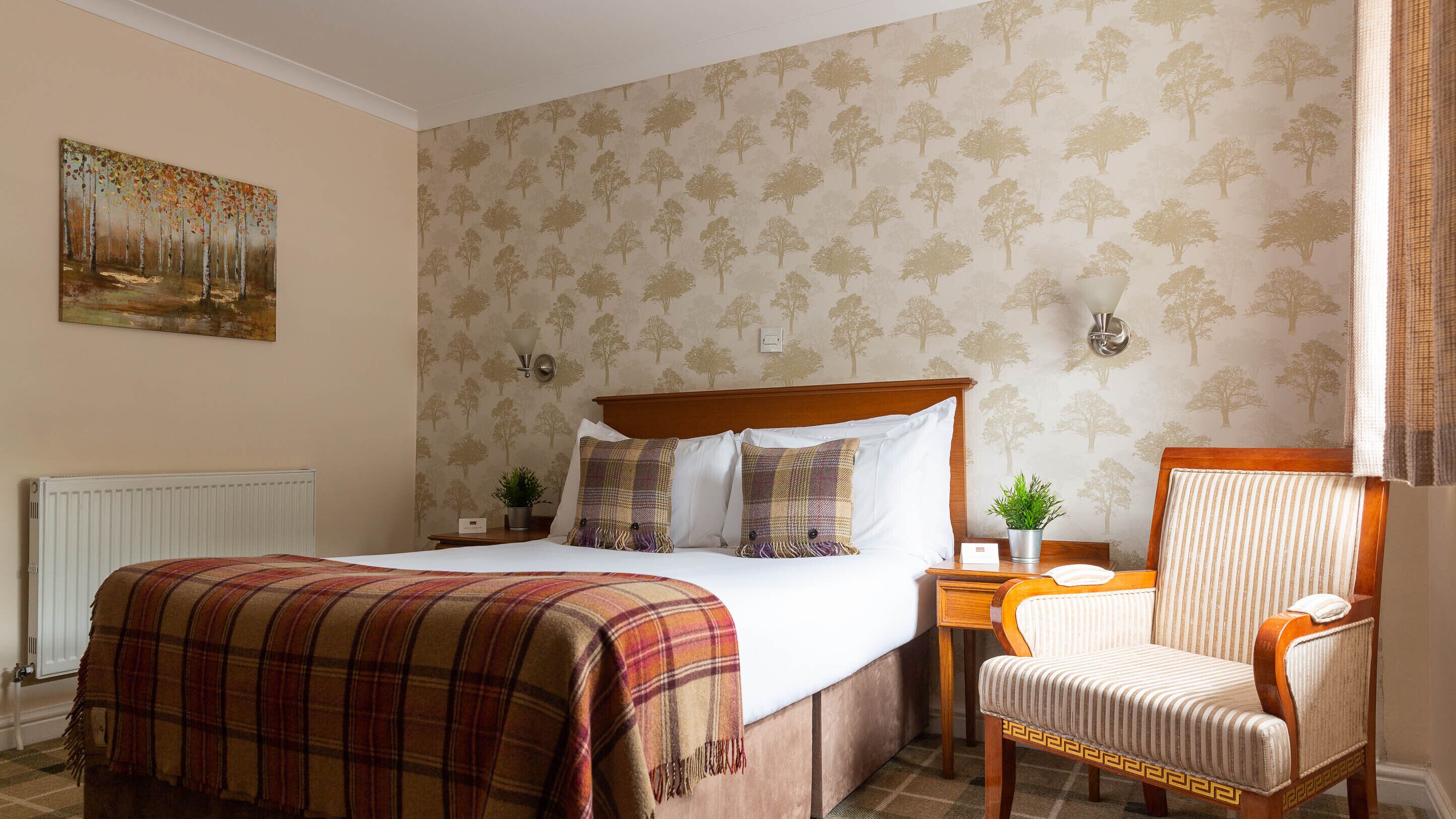 A hotel room with a bed, a chair, a nightstand, and a painting on the wall.