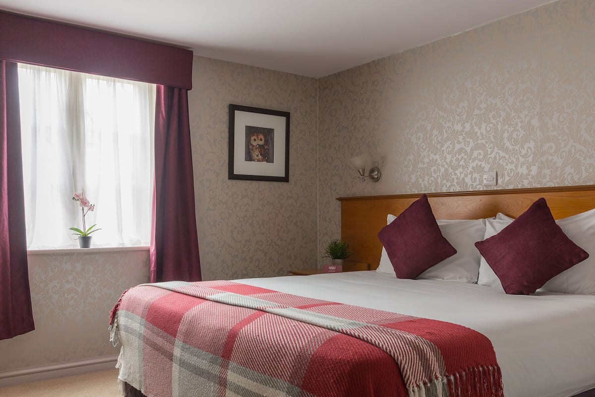 A neatly made bed with a checkered blanket, two pillows, and a window with curtains.
