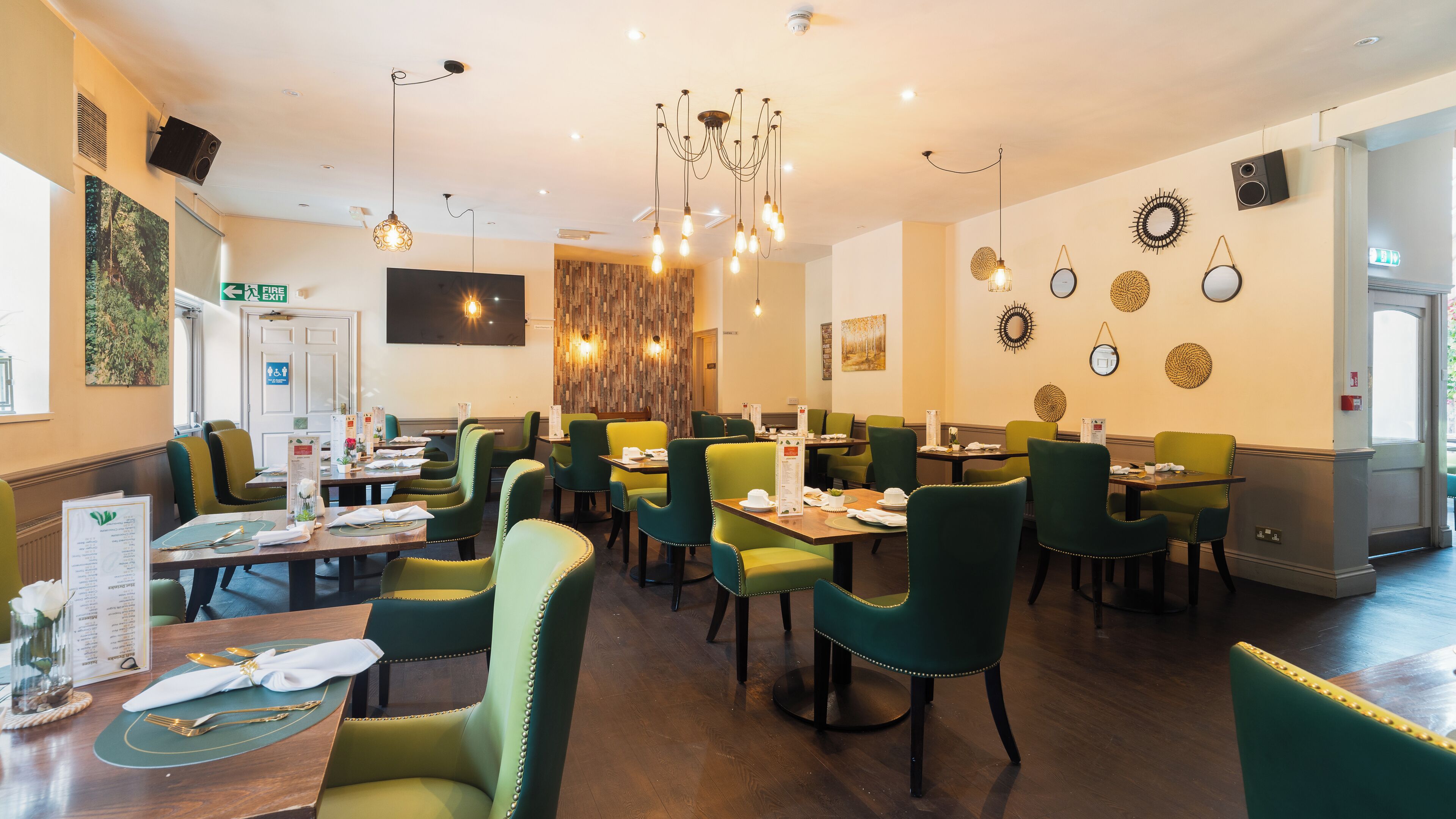 A restaurant with green upholstered chairs, wooden tables, and a chandelier.
