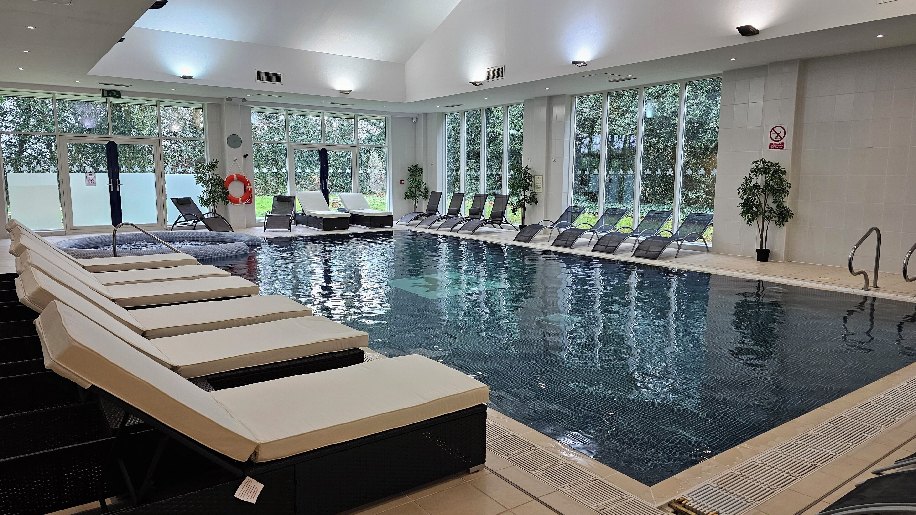 An indoor swimming pool with lounge chairs, a hot tub, and large windows.