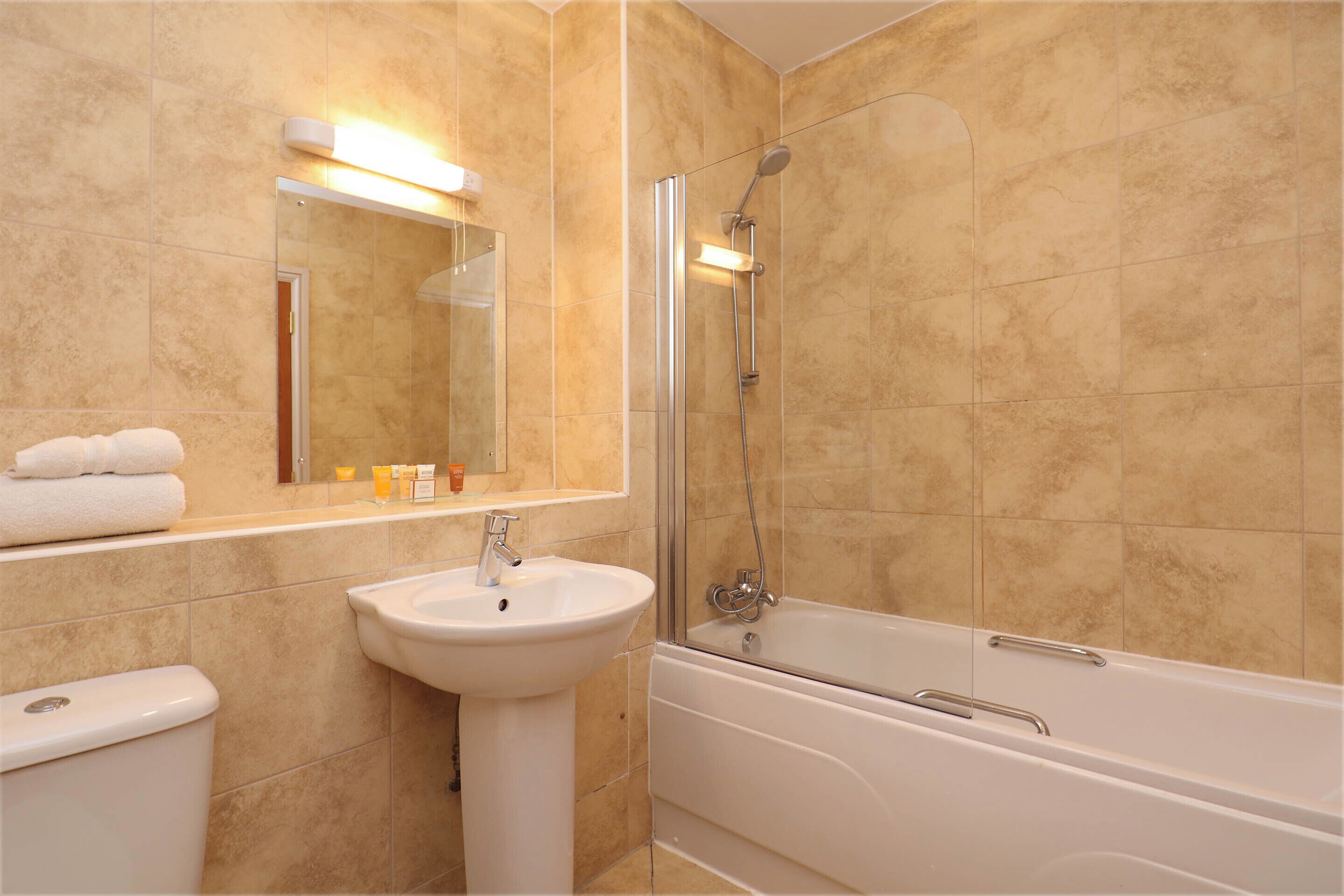 Un baño con baldosas color crema, un lavamanos blanco, un espejo, un inodoro y una bañera.