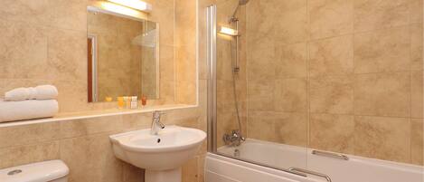 Un baño con baldosas color crema, un lavamanos blanco, un espejo, un inodoro y una bañera.