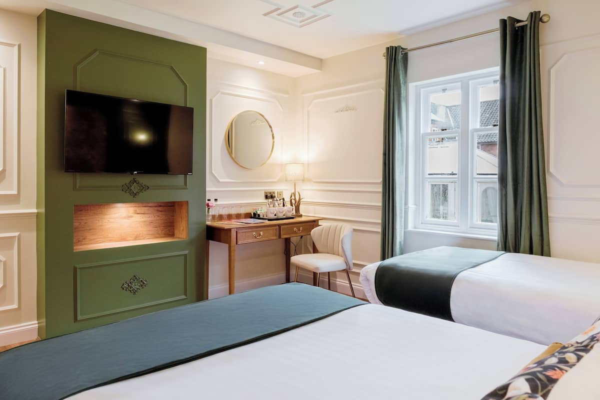 A hotel room with two beds, a desk with a chair, a television, a mirror, and a window with curtains.