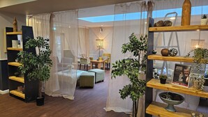 Una sala de estar moderna con un sofá, una mesa de comedor y sillas. Hay plantas y objetos decorativos en estantes.