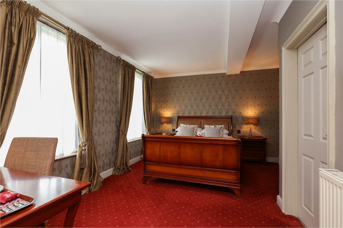 A bedroom with a wooden bed, two bedside lamps, a chair, and a table.