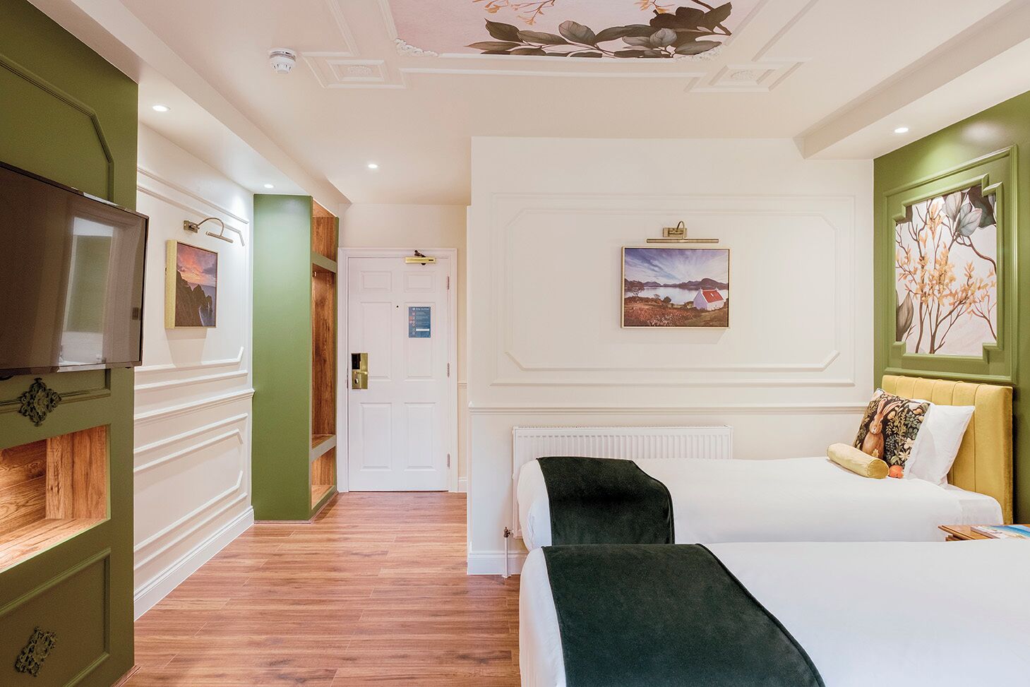 Hotellihuone, jossa on sänky, televisio, taulu ja ovi.
