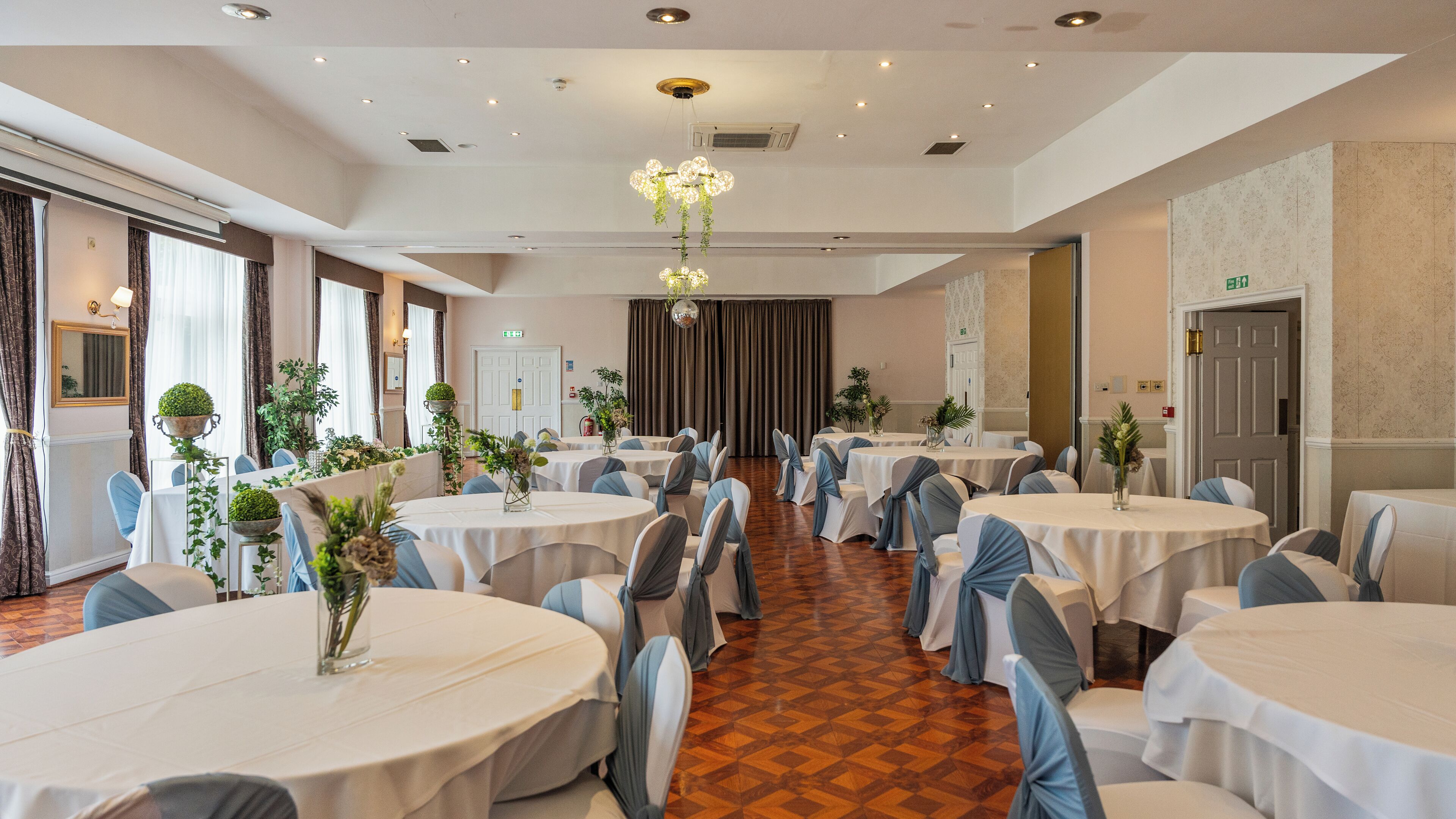 A banquet hall with round tables, chairs, and a chandelier.