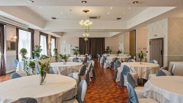 A banquet hall with round tables, chairs, and a chandelier.