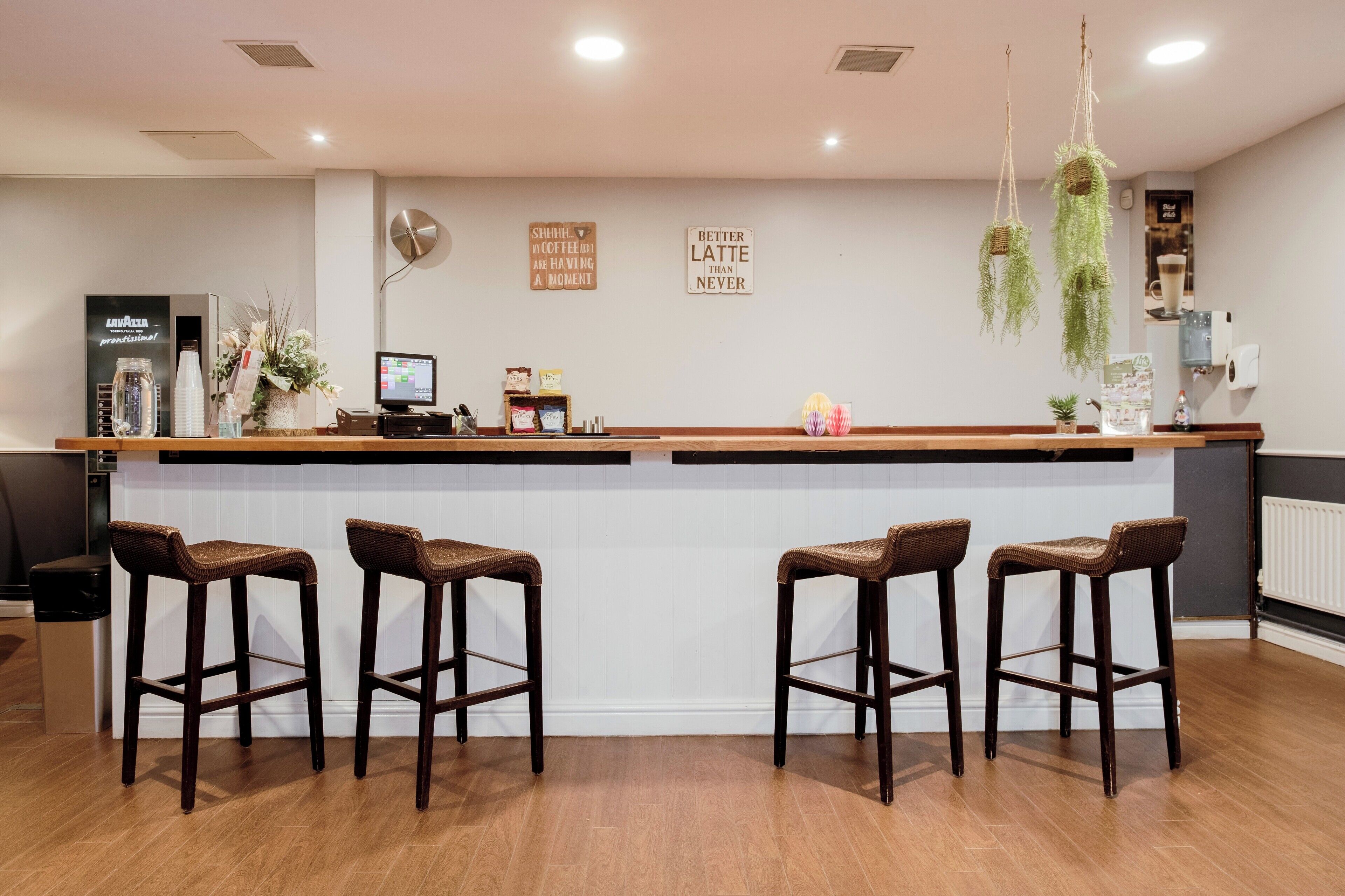 A bar area with a white countertop, four wicker bar stools, a computer monitor, and decorative items like a clock and wall art.