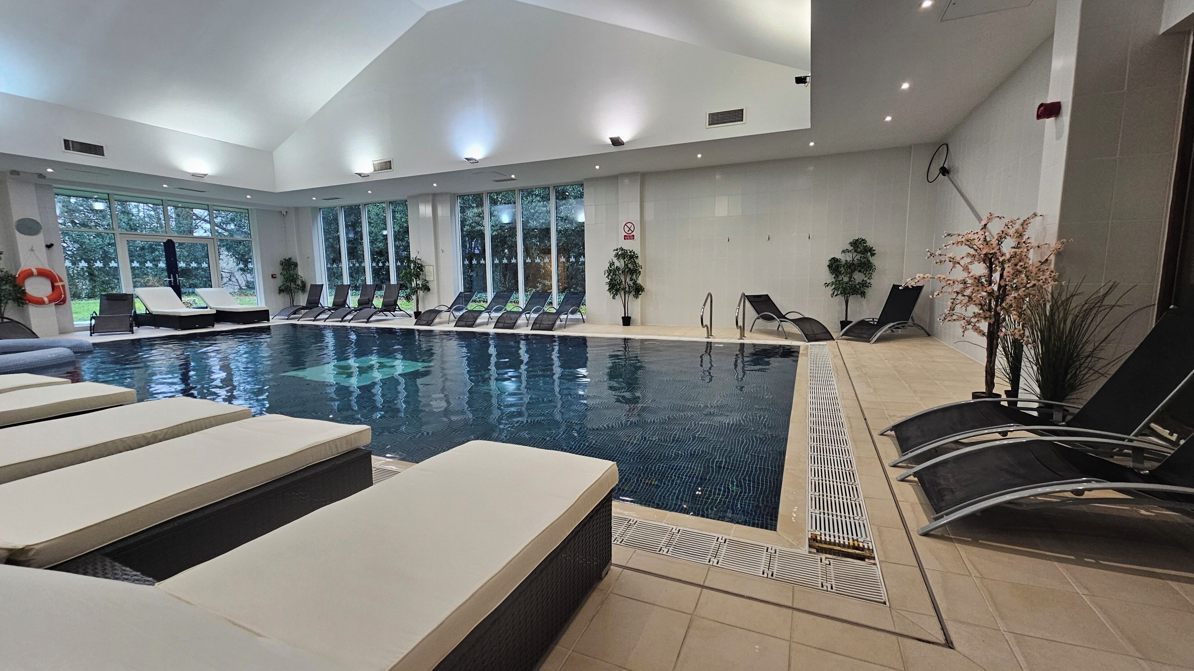 An indoor swimming pool with lounge chairs and potted plants.