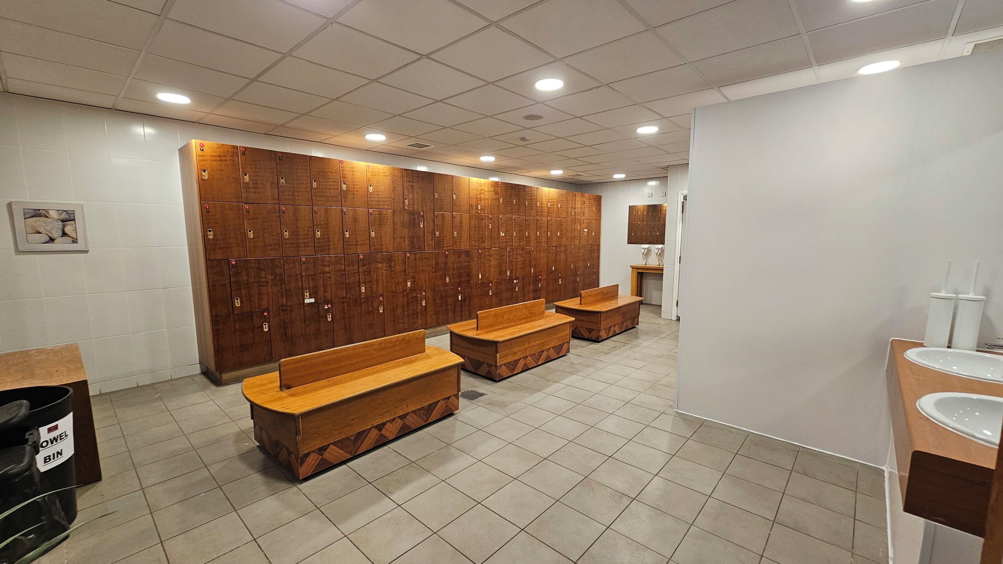 A public restroom with wooden benches, a sink, and a row of lockers.