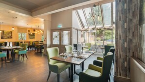 Un restaurante con varias mesas y sillas, ventanas amplias y un techo alto.