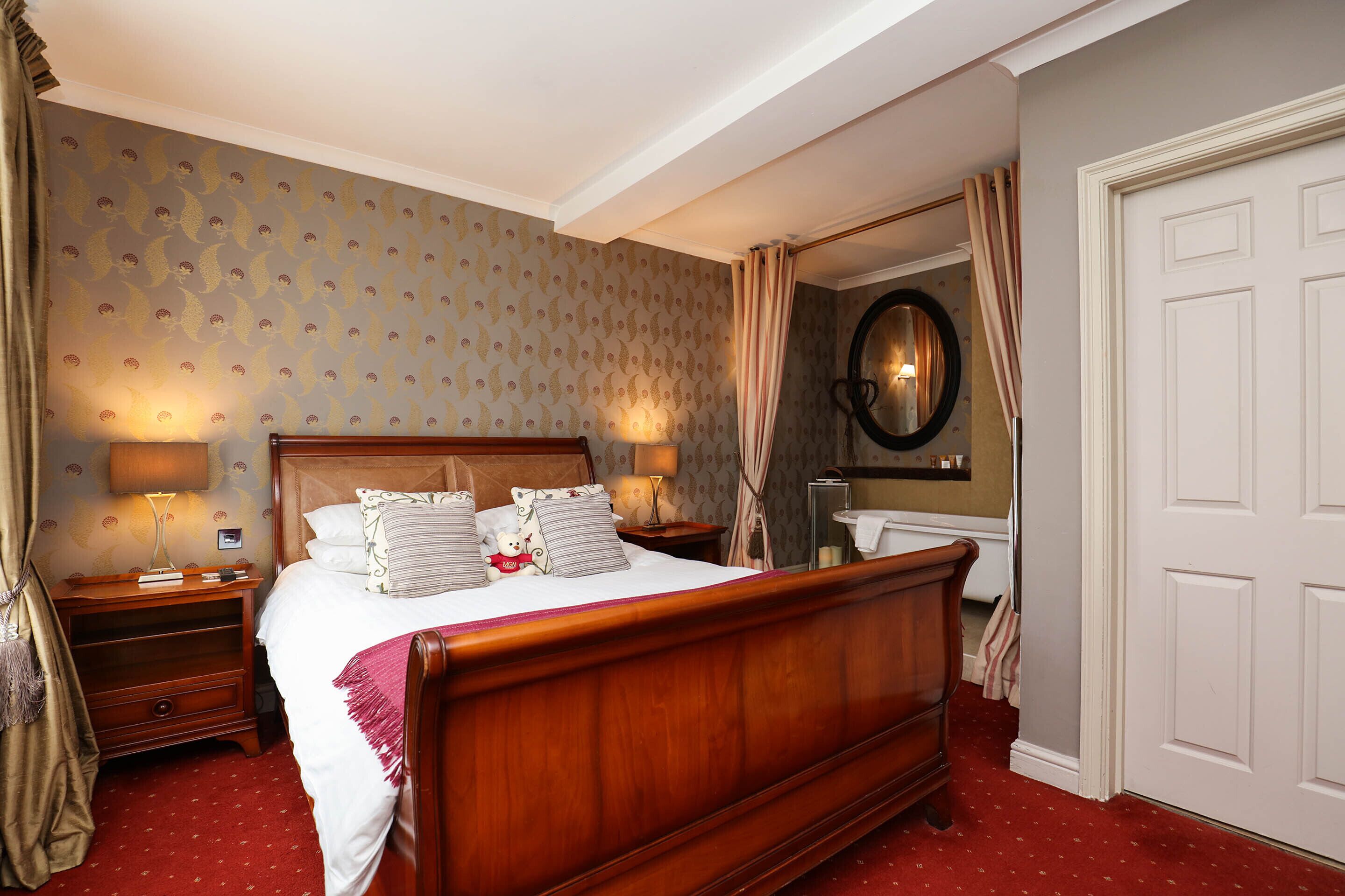 A neatly arranged bedroom with a wooden bed, two bedside tables with lamps, a mirror, and a door.