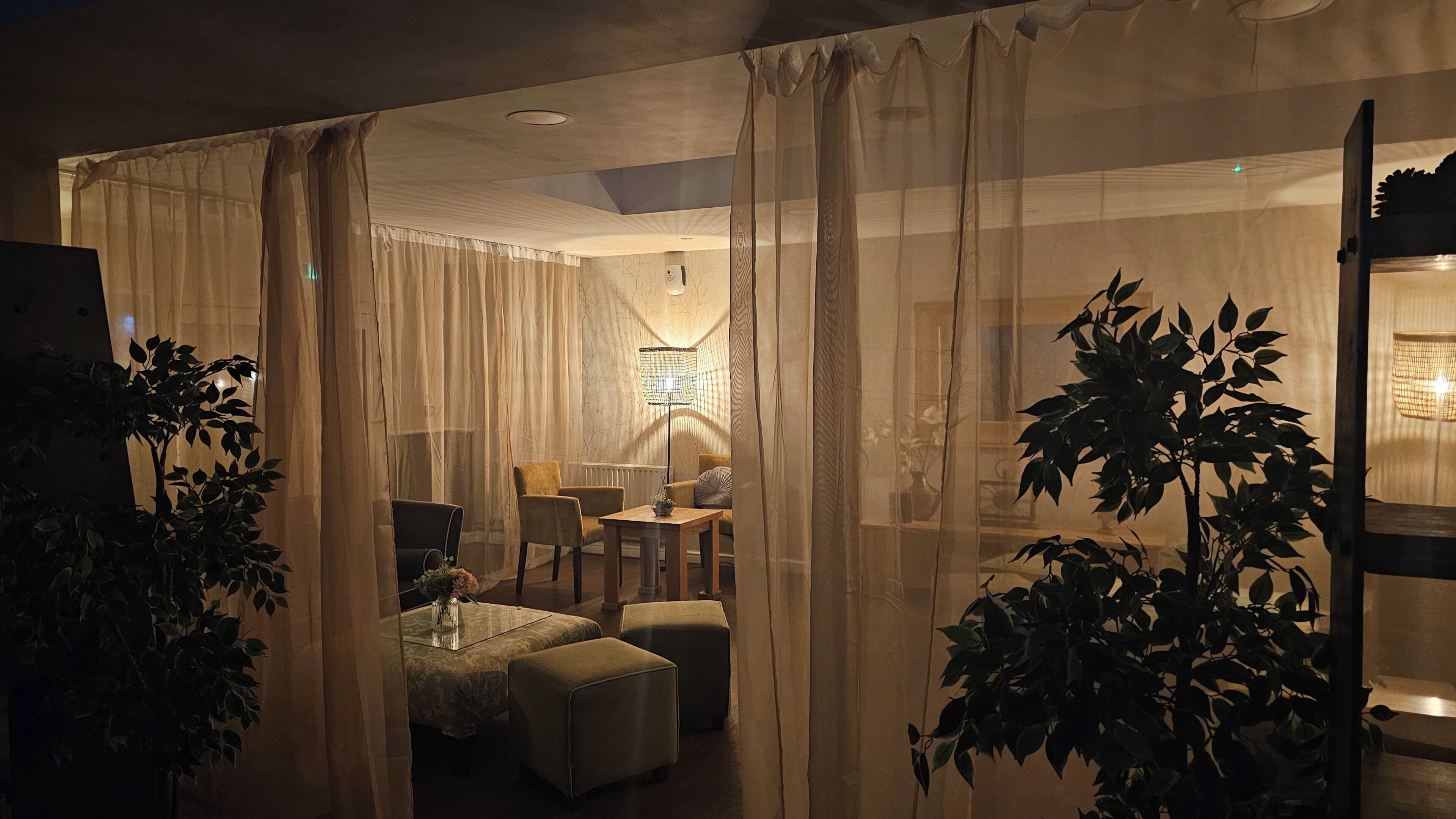 A room with a glass partition, a table with a vase, and a chair.