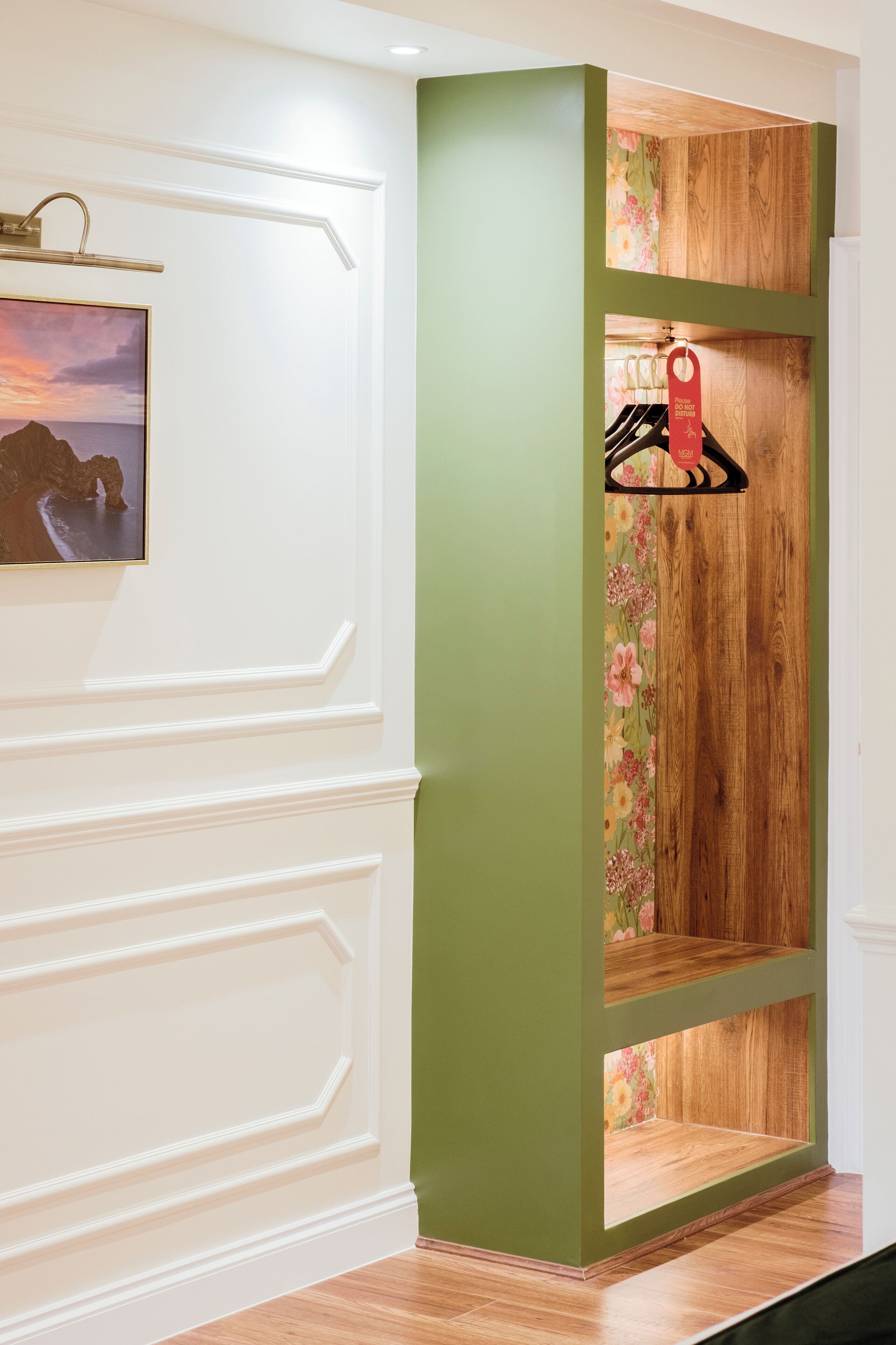 Un pasillo con una pared verde decorativa, estanterías de madera y un cuadro enmarcado a la izquierda.