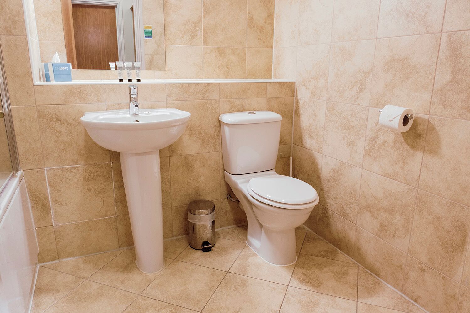 A bathroom with a pedestal sink, a toilet, and a trash bin.