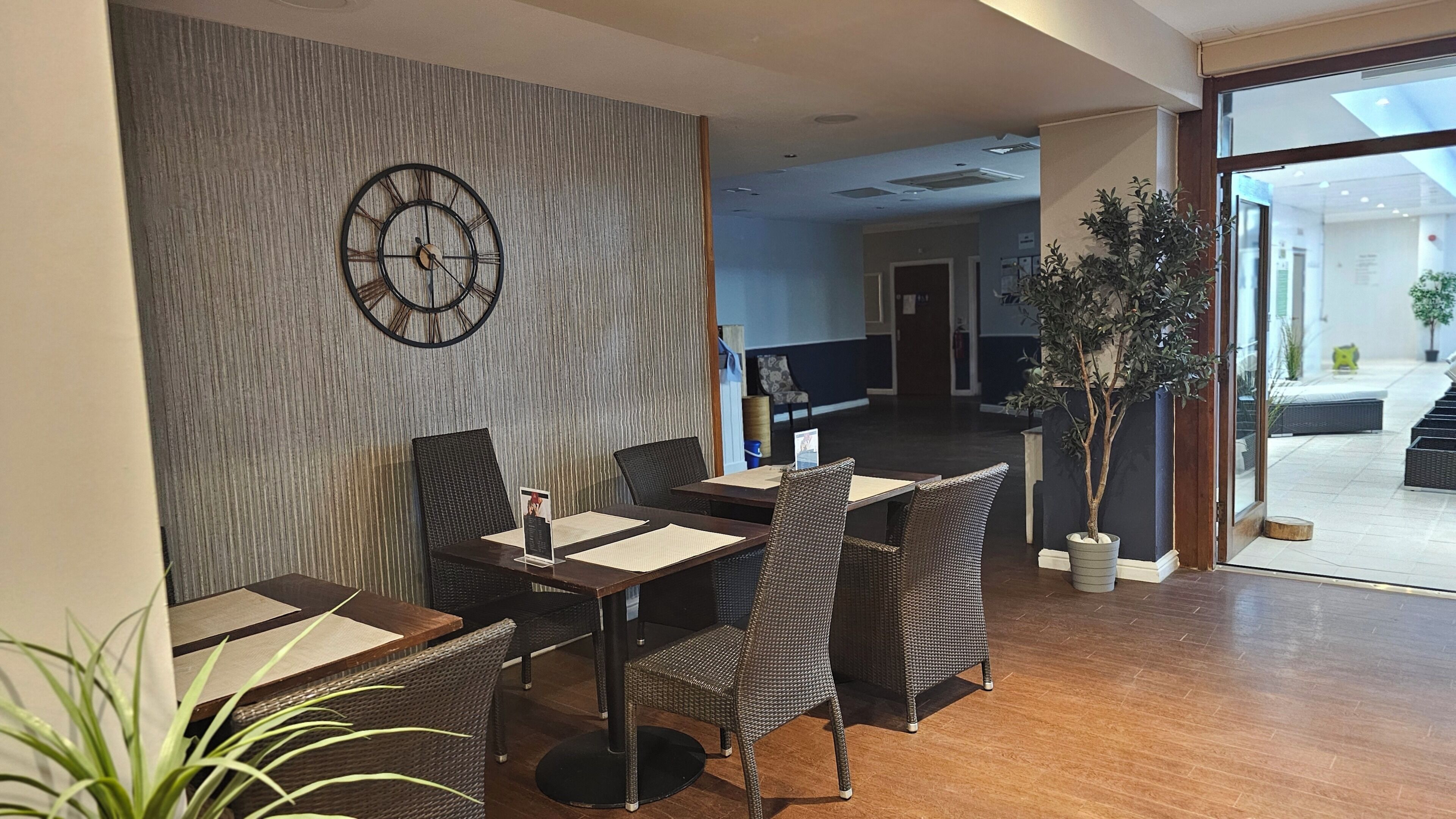 A restaurant with wicker furniture, a wall clock, and a view of the outdoor area.