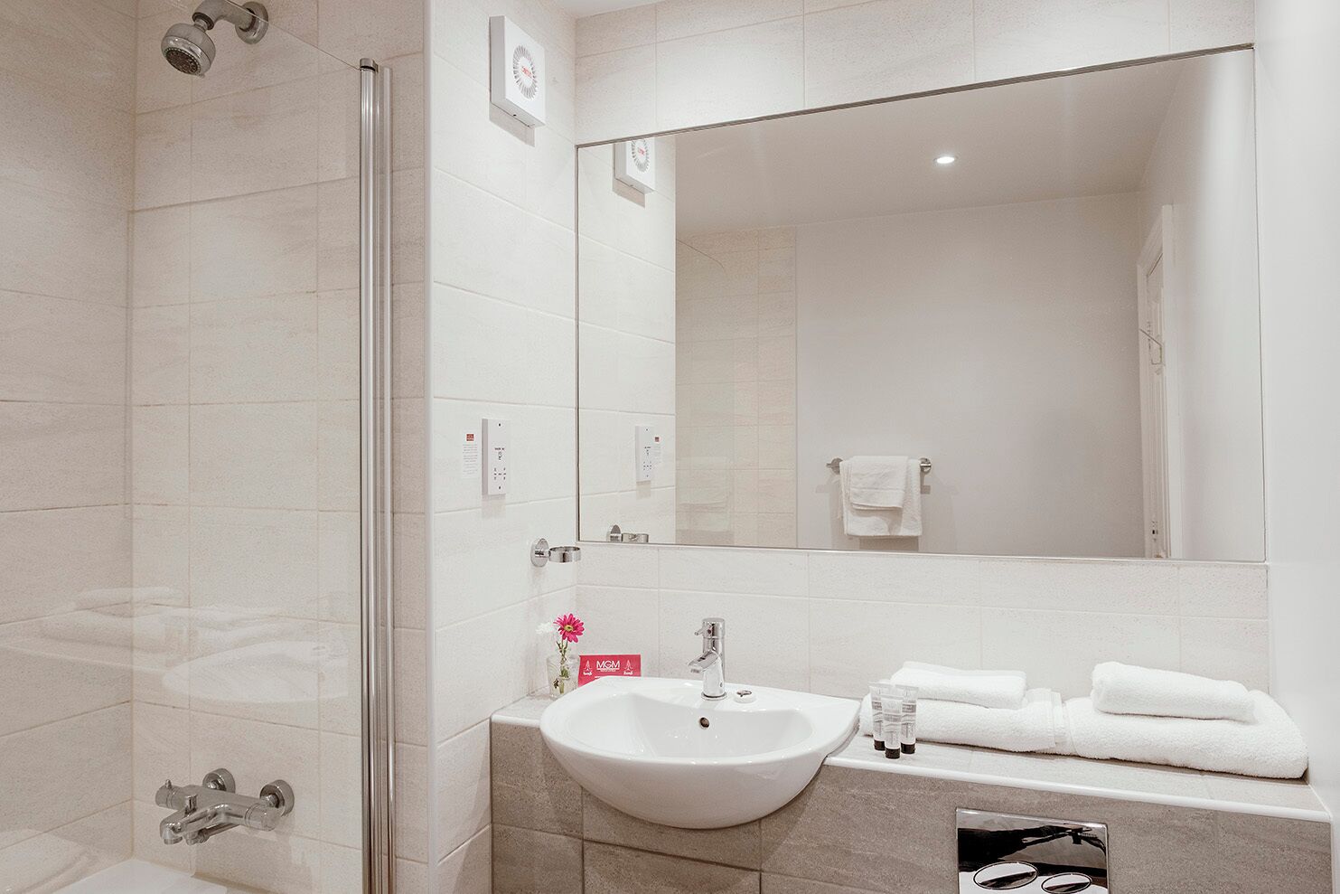 A modern bathroom with a glass shower enclosure, a sink with a mirror above it, and a towel rack with folded towels.