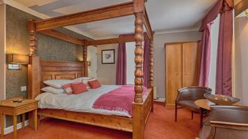 A four-poster bed with a wooden headboard, a bedside table, a chair, a small table with a bowl, and a wardrobe.