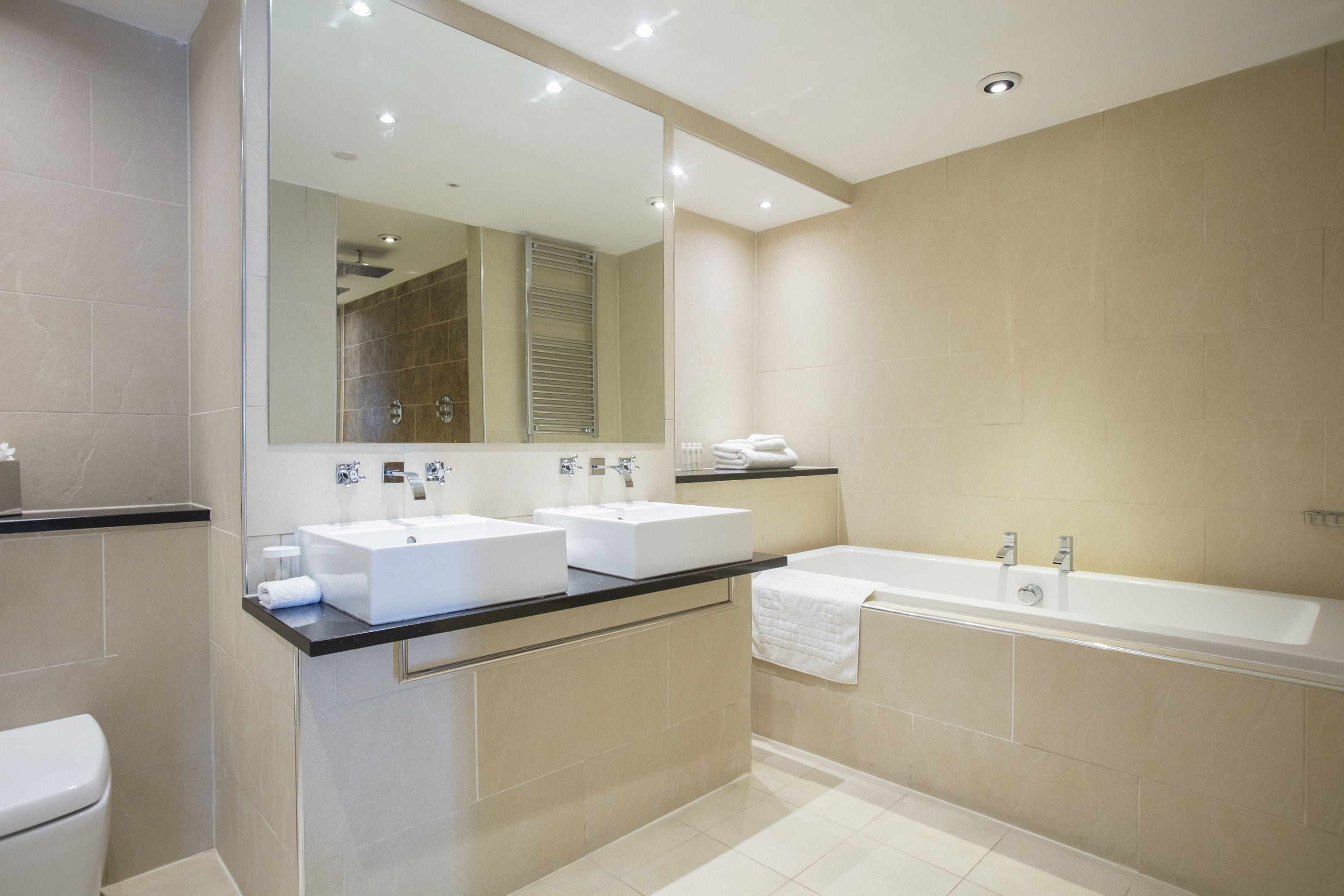 Un baño moderno con dos lavamanos, una bañera y un espejo grande.