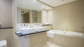 Un baño moderno con dos lavamanos, una bañera y un espejo grande.