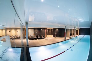 Une piscine intérieure avec des couloirs de nage clairement délimités, un espace d’accueil doté de sièges et un design architectural moderne.