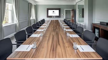 A conference room with a long wooden table, black chairs, and a large screen displaying the DoubleTree logo.