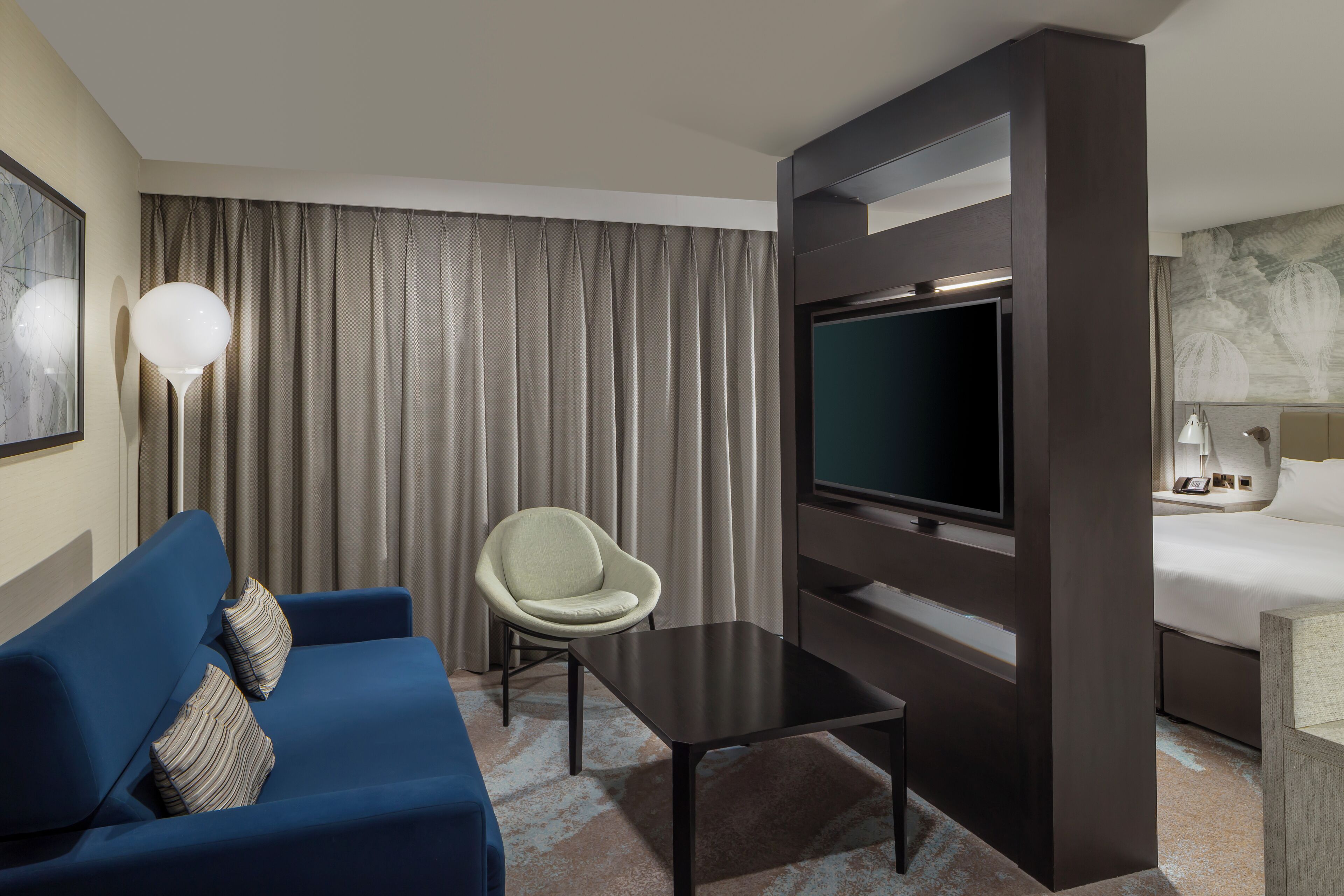 Ein Hotelzimmer mit blauem Sofa, einem kleinen Tisch, einem Fernseher, einem Sessel und einem Bett.