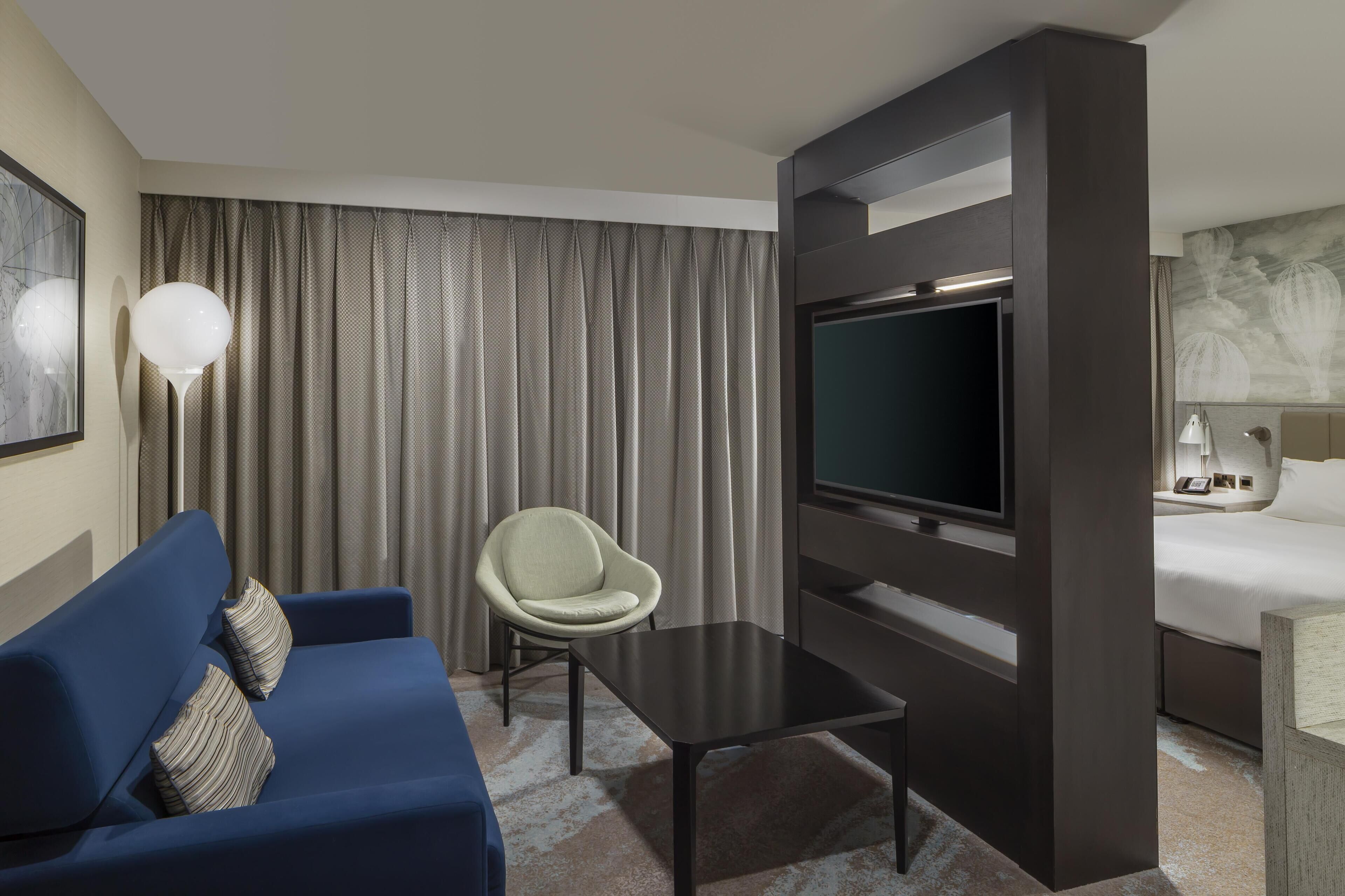 Una camera d'albergo con un divano blu, un tavolino, una televisione, una sedia e un letto.