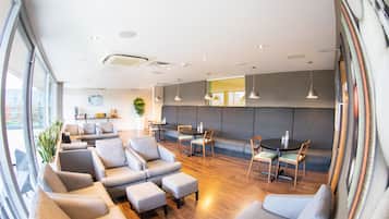 Ein modernes Interieur mit Sofas, Sesseln, einer Essecke und einem großen Fenster, das für natürliches Licht sorgt.