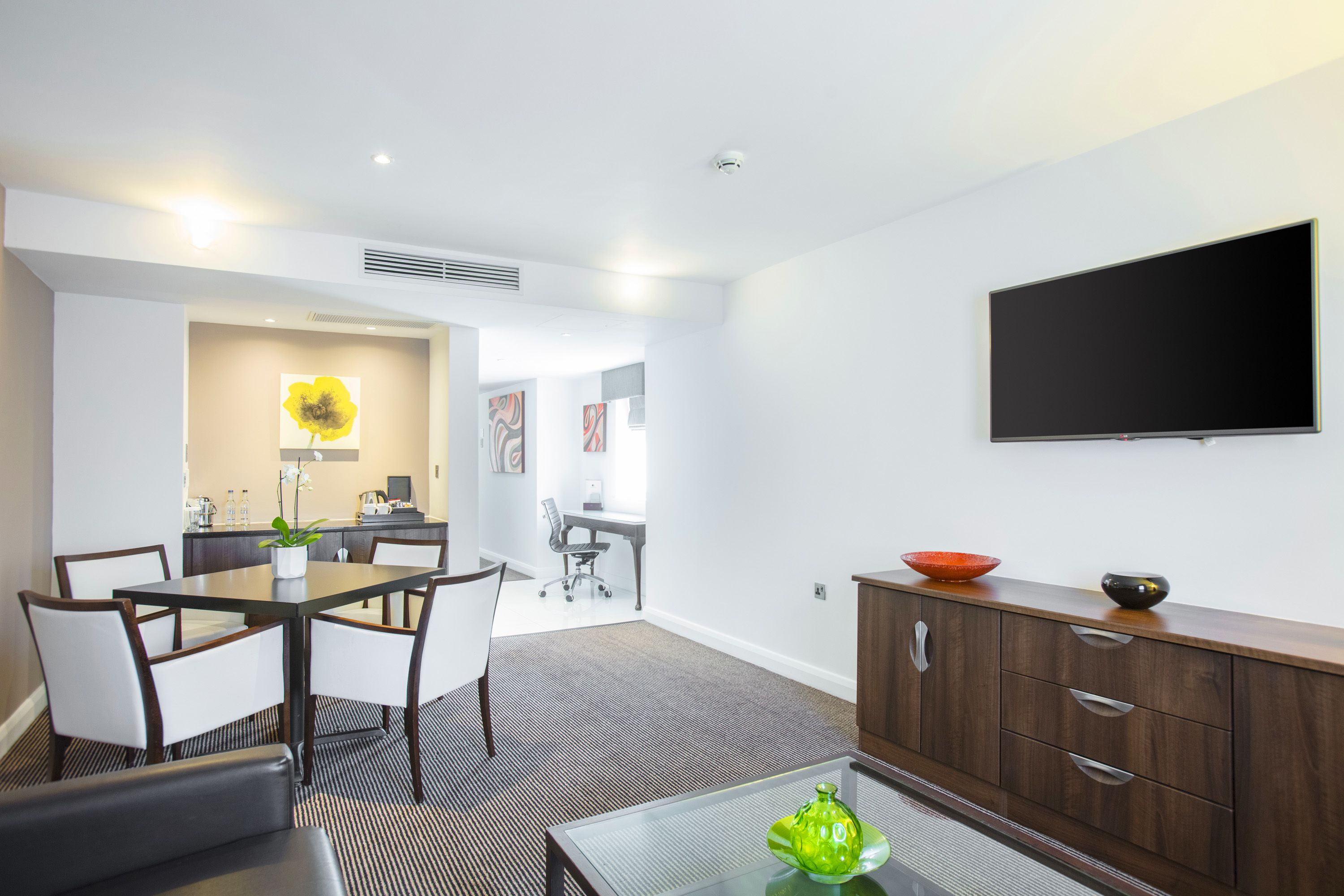 A modern hotel room with a dining area, a flat-screen TV, and a wooden cabinet.